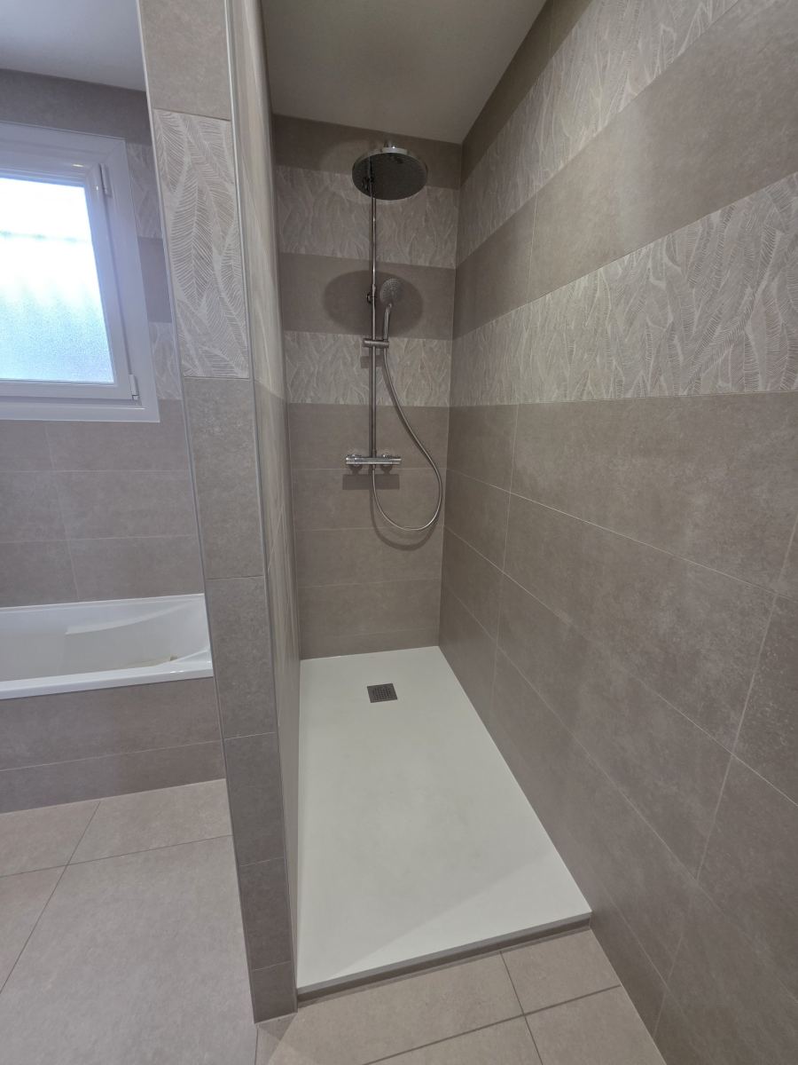 Douche avec receveur extra-plat et colonne thermostatique à côté d'une baignoire